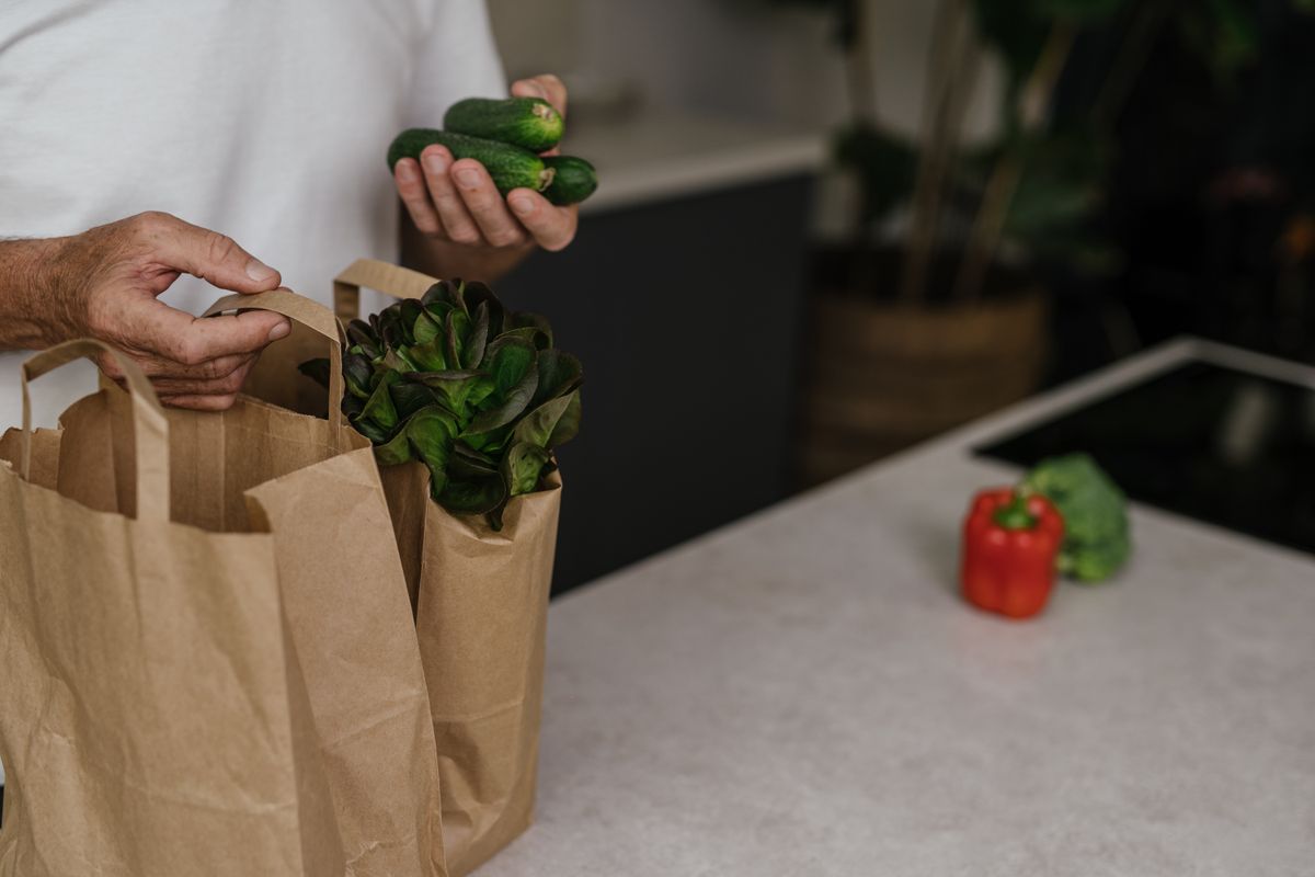 Iemand pakt verse groenten uit een papieren boodschappentas